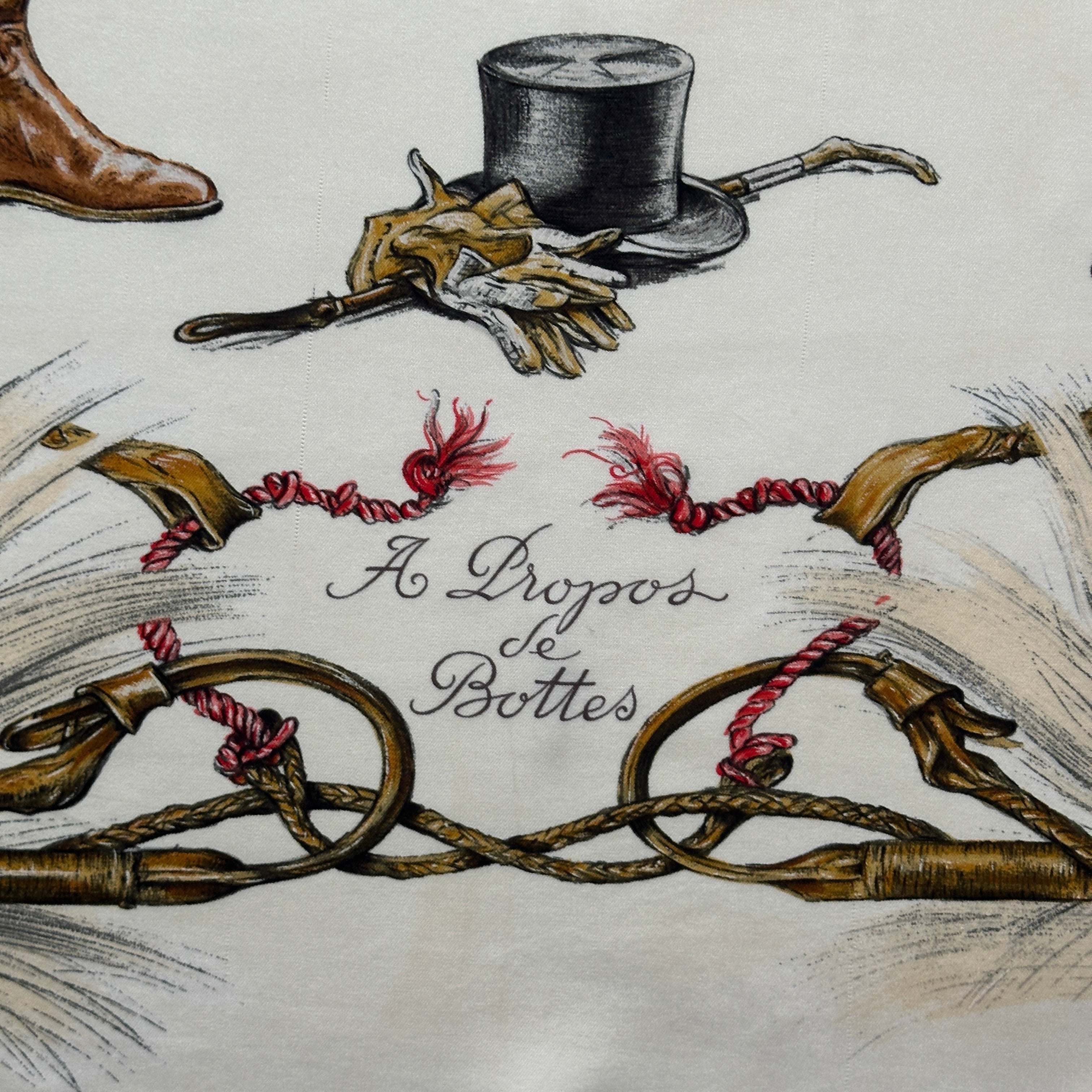 Calligraphie du titre "A Propos de Bottes" entourée de cravaches tressées et gants de cuir sur soie crème.