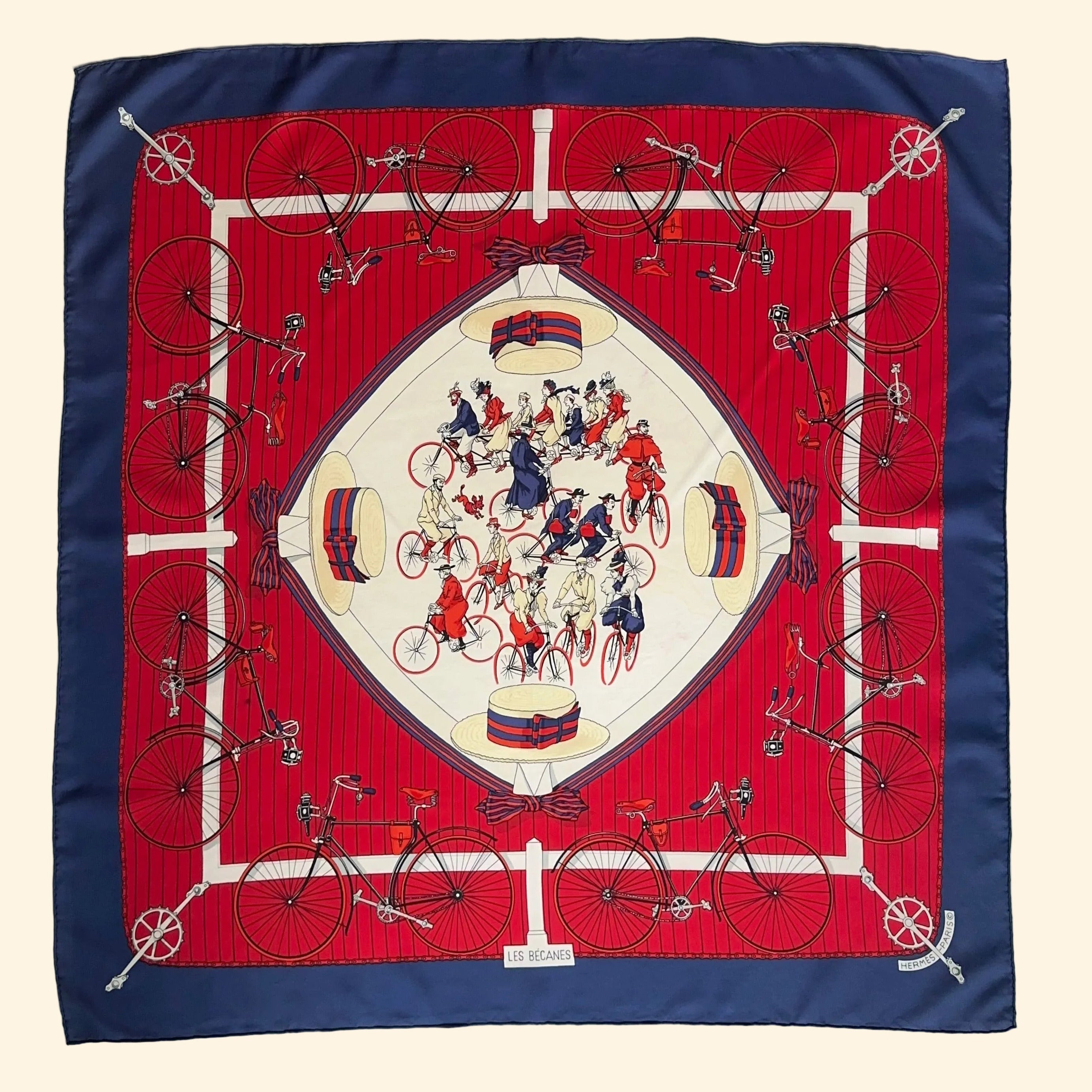 Le foulard Hermès Les Bécanes déployé à plat, montrant la bordure marine, le fond rouge rayé et le centre blanc animé.
