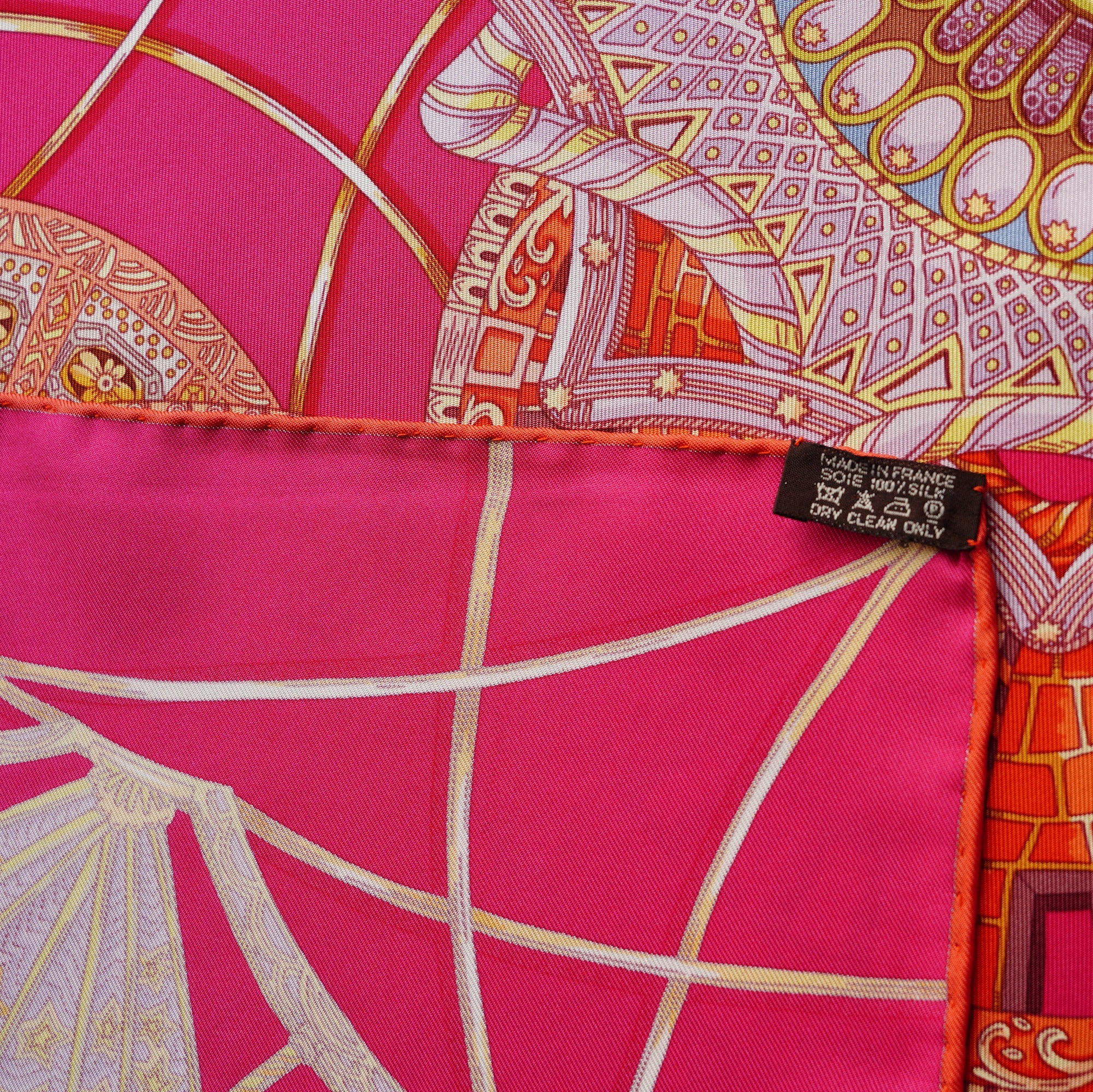 Détail technique sur l'angle du carré, montrant le roulotté contrasté orange Hermès gonflé, l'étiquette de composition présente et la signature de la maison.