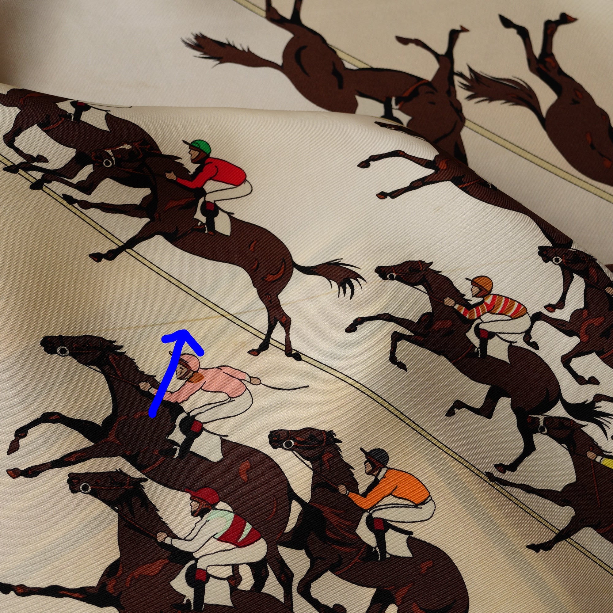 Porté du carré Hermès "Les Courses" plié en cravate, mettant en valeur les jockeys et les bandes graphiques.