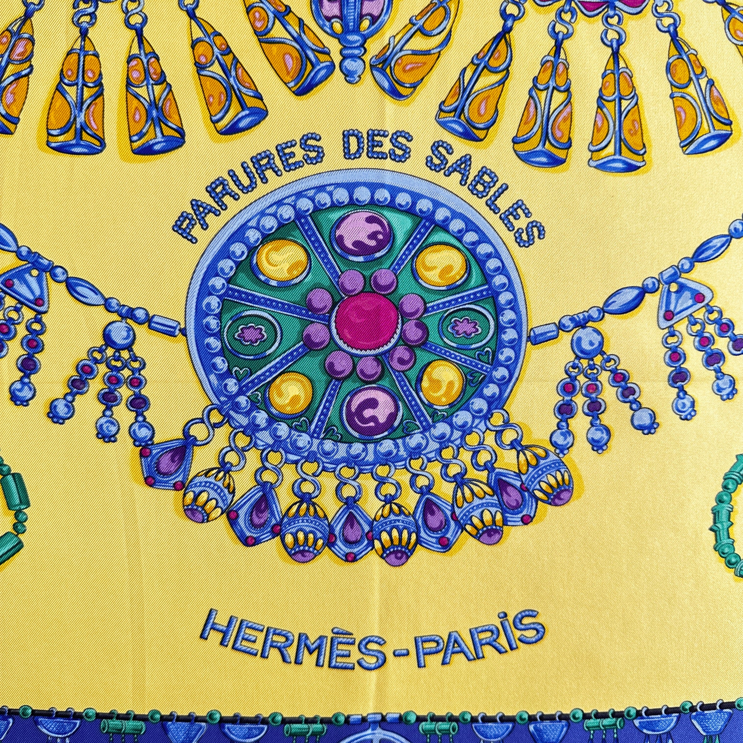 Inscription du titre Parures des Sables entourée de colliers d'or et de perles.